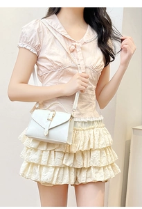 Close-up of stylish white crossbody bag with gold buckle on a light pink outfit