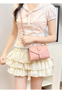 Detailed view of pink crossbody bag with gold buckle on elegant pleated skirt outfit