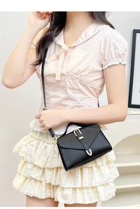 Detail of black crossbody bag featuring a golden U-shaped buckle on envelope flap cover