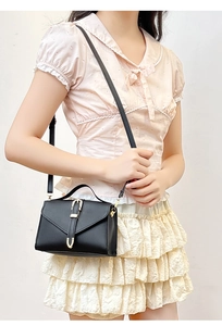 Detail view of a black mini crossbody bag with a gold U-shaped buckle on a floral outfit