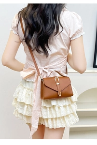 Close-up of brown leather crossbody bag with gold U-shaped buckle on a female model