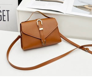 Detailed close-up of brown litchi pattern leather bag with gold buckle on white surface