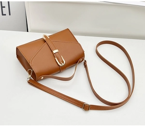 Detail of a brown leather crossbody bag with a sleek gold metal buckle on the front