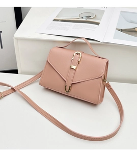 Detailed side view of a soft pink square leather handbag with metallic buckle on white table