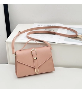 Pink crossbody bag with V-shaped flap and golden U-shaped buckle detail on a white pedestal