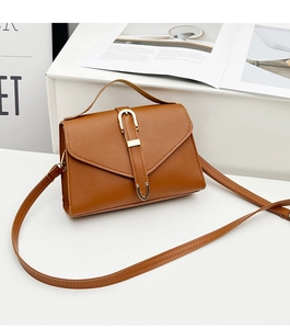 Detailed view of caramel PU leather handbag with gold buckle and top handle on white stand
