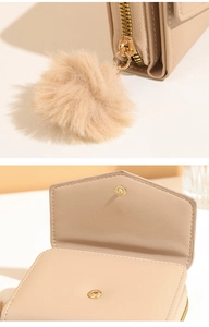 Detail of beige trifold wallet featuring a plush pom-pom charm and golden hardware snaps