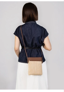 Detail of woven straw crossbody bag with brown leather trim and golden zipper