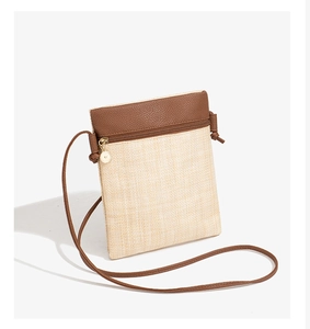Close-up of small woven straw phone bag with brown leather trim and golden metal zipper