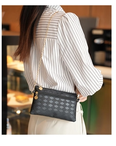 Close-up of black rhombic pattern handbag with gold chain strap and metal charm detail