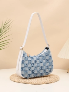 Detail of blue and white checkered denim underarm bag with frayed tassel edges on a straw mat
