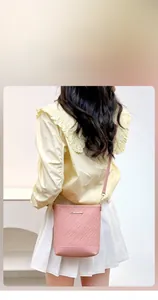 Close-up of pink embossed bucket bag with gold logo on a model in a summer outfit