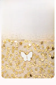 Détail de la pochette à paillettes dorées avec papillon décoratif en émail blanc