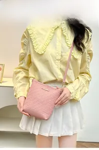 Close-up of pink textured crossbody bag featuring metallic logo and slender shoulder strap