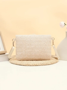 Detail of cream straw crossbody bag with V-pattern weaving on a rustic wooden background