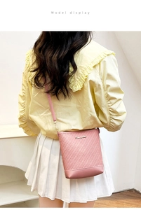 Pink woven crossbody bag with flat base and metal logo plate worn by a model