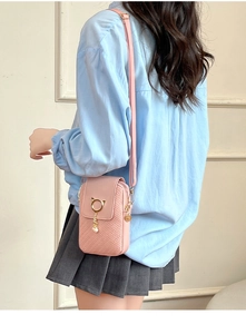 Detail of pink crossbody phone bag featuring woven texture and gold cat-ear pearl pendant