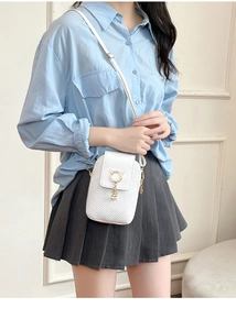 Close-up of white embossed phone bag featuring golden cat buckle and pearl pendant detail