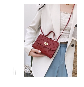 Detail showing the burgundy quilted handbag with a gold-tone twist lock on white blazer