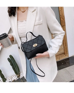 Close-up of black quilted small square handbag with gold hardware and top handle worn by model