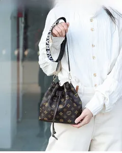 Detail of drawstring bucket bag featuring brown monogram pattern and wide logo strap