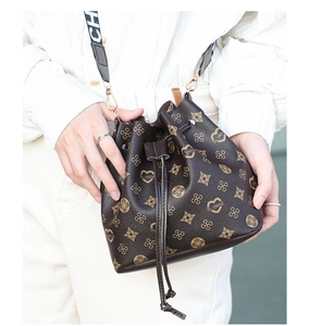 Detail of drawstring bucket bag with monogram pattern and wide lettered strap