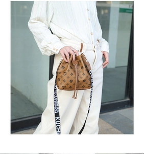 Brown leather drawstring bucket bag with floral monogram and wide woven shoulder strap