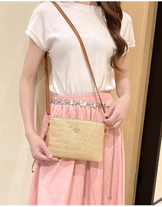 Détail du sac bandoulière en paille tressée avec logo fleur dorée et sangle brune