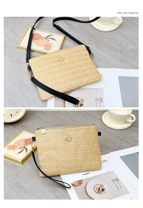 Détail d'une pochette enveloppe en paille beige avec logo doré et bandoulière en cuir noir
