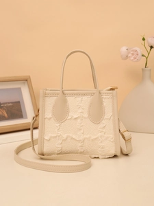 Detail of cream woven tote bag with leather trim and gold zipper on warm background