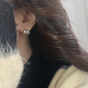 Primo piano di orecchini a triplo cerchio in argento indossati da una modella con maglione