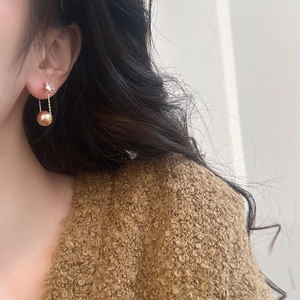 Detail of gold tassel earrings with hanging pearl on model wearing a brown sweater