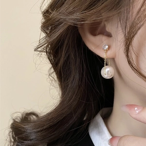 Macro shot of long gold tassel earring with sparkling zircon and glossy white pearl