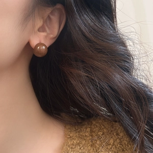Close-up of a caramel brown round stud earring with a glossy finish on a model