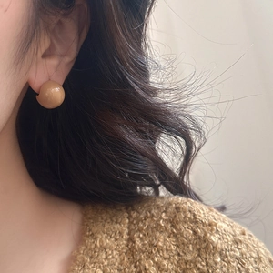 Close-up of polished glossy sphere stud earrings in warm brown finish on model
