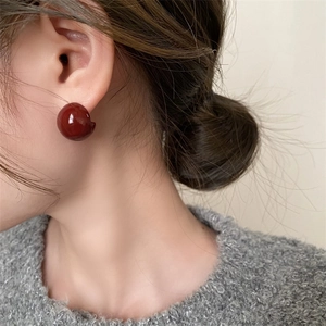 Close-up of deep red spherical stud earrings with glossy finish on a model's ear