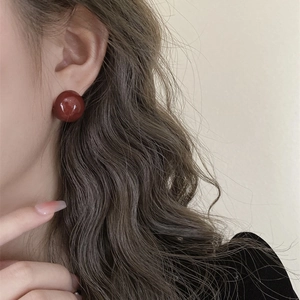 Close-up of a model wearing a glossy deep red spherical stud earring with vintage style