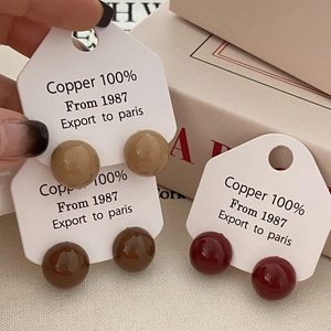 Detailed close-up of glossy copper ball stud earrings in earthy khaki and red tones