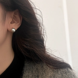 Close-up of 10-12mm grey round pearl stud earrings with metallic luster on model ear