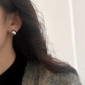 Close-up of minimalist silver spherical stud earring worn by model in soft light