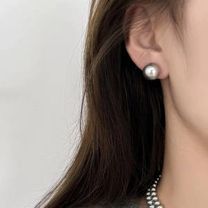 Close-up of a large round grey pearl stud earring with high metallic luster on model