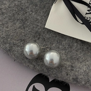Macro shot of large gray pearl stud earrings with metallic luster on gray felt surface