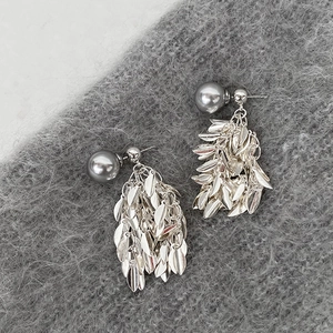 Macro detail of silver leaf tassel earrings with dark grey pearl on plush grey fabric