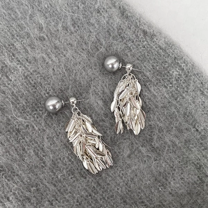 Detail of silver leaf tassel earrings with gray pearl stud on soft fabric background
