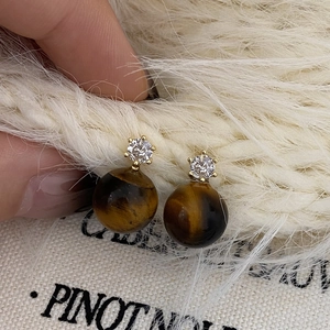 Close-up of tiger eye stone earrings with cubic zirconia and gold plating on fur background