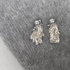 Detailed view of silver leaf tassel earrings with grey pearls on soft knit fabric