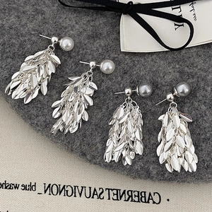 Detailed view of leaf tassel earrings with white and dark gray pearls on textured fabric