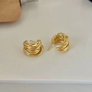 Détail de boucles d'oreilles clous dorées multicouches entrelacées en forme de C