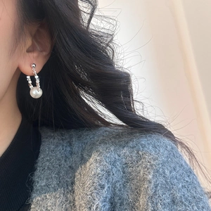 Boucles d'oreilles argentées en U avec perle blanche sur mannequin en manteau