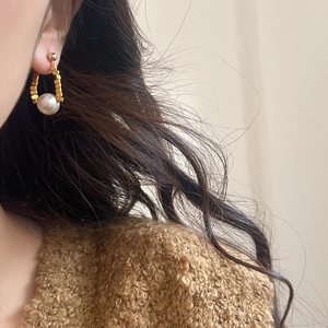 Détail d'une boucle d'oreille élégante en perles et cubes dorés portée par un mannequin